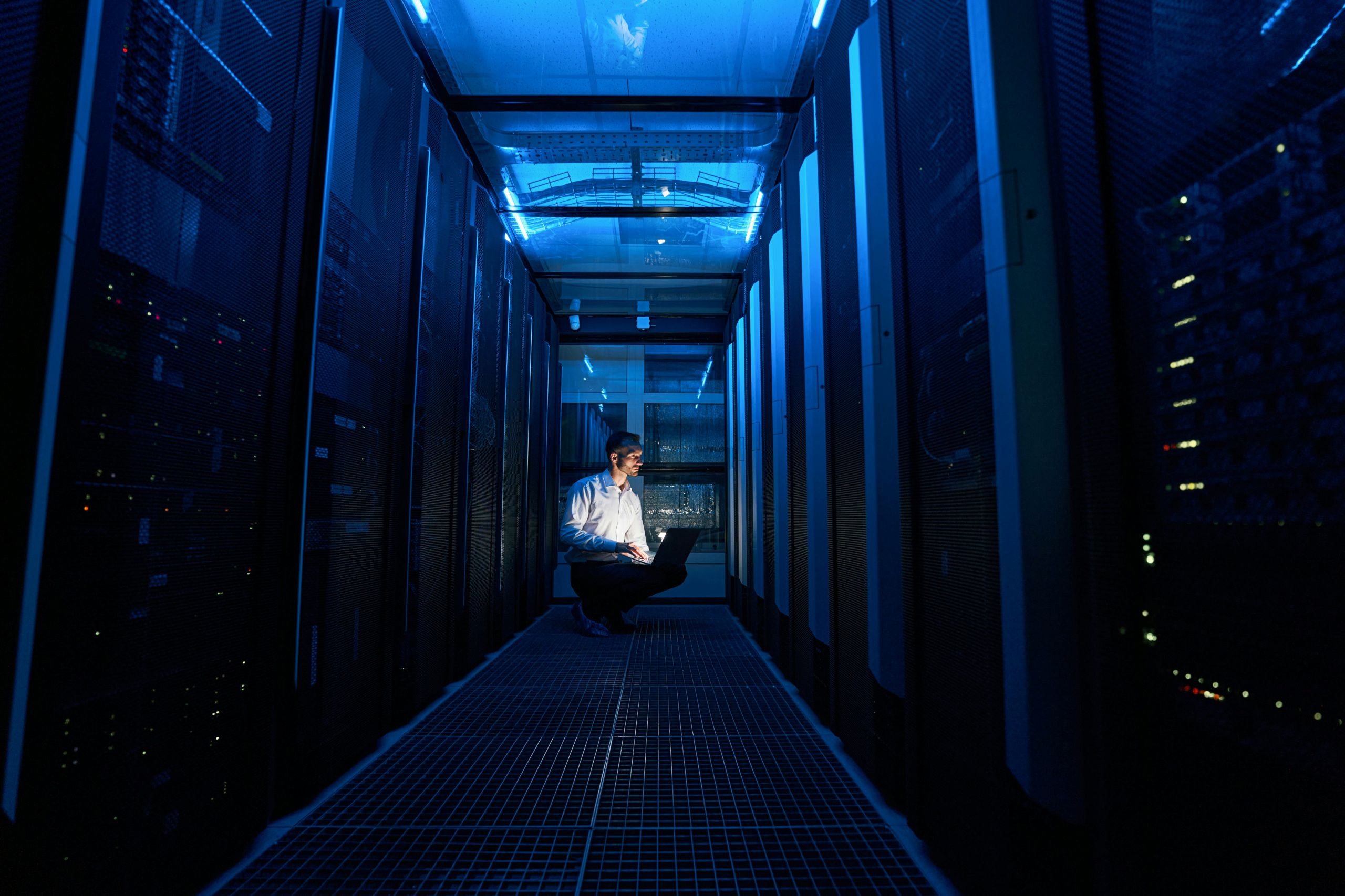 IT-Techniker arbeitet mit einem Laptop im blau beleuchteten Serverraum eines Rechenzentrums