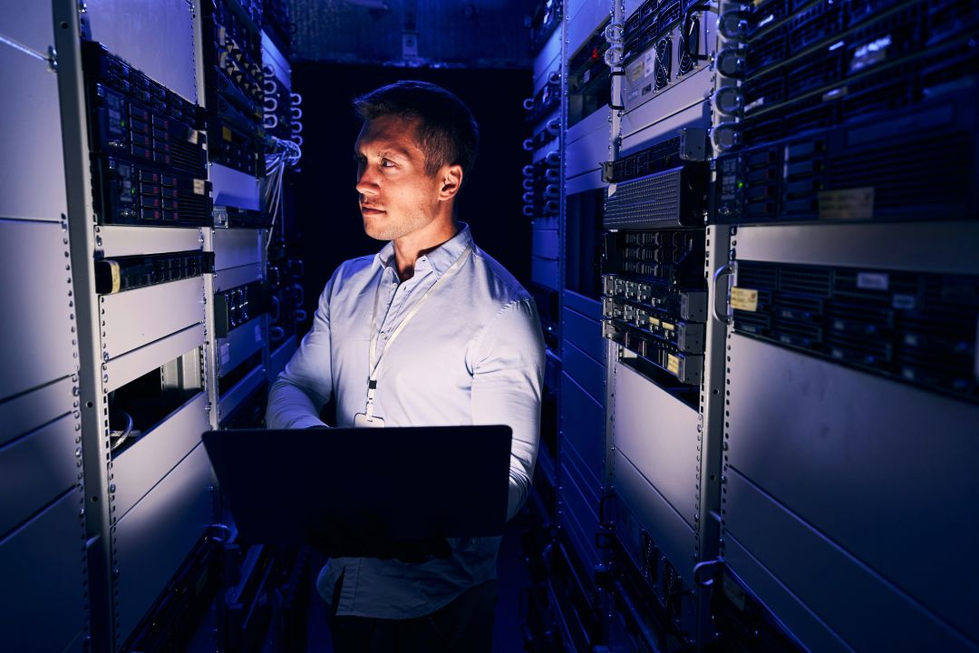 Ein Man steht in einem Serverraum, wo er die Performance der IT verbessert.
