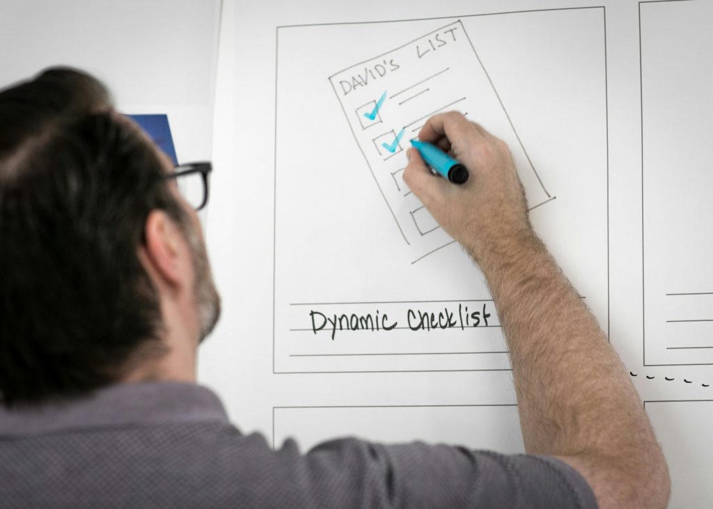 Mann zeichnet Dynamic Checklist auf Papier – UI-Wireframe Planung mit blauem Marker
