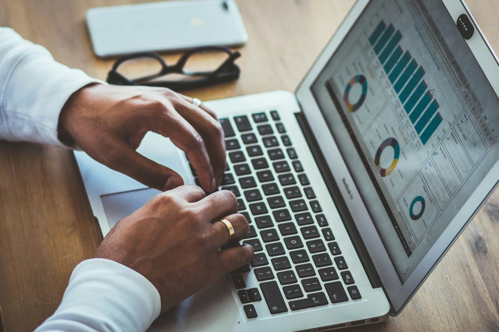 Hände tippen auf einem Laptop, auf dessen Bildschirm ein Analyse-Dashboard mit Balken- und Kreisdiagrammen zu sehen ist