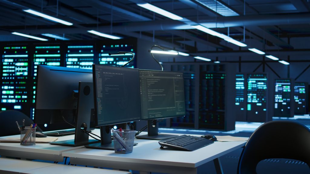 Arbeitsplatz mit zwei Monitoren und Code-Editor vor Serverschränken in einem beleuchteten Rechenzentrum