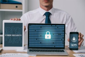 Geschäftsmann präsentiert Tablet, Laptop und Smartphone mit Anzeigen zu Cybersicherheit, Schloss-Symbol und DSGVO-Konformität