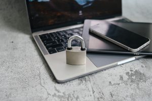 Vorhängeschloss liegt auf einer Laptop-Tastatur neben Tablet und Smartphone als Symbol für Gerätesicherheit