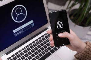 Hand hält Smartphone mit Sperrbildschirm-Icon vor einem Laptop mit Anmeldemaske für Benutzername und Passwort